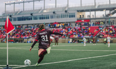 AFC Toronto player Colby Barnett takes a corner kick. Fans occupy the stands in front of her.