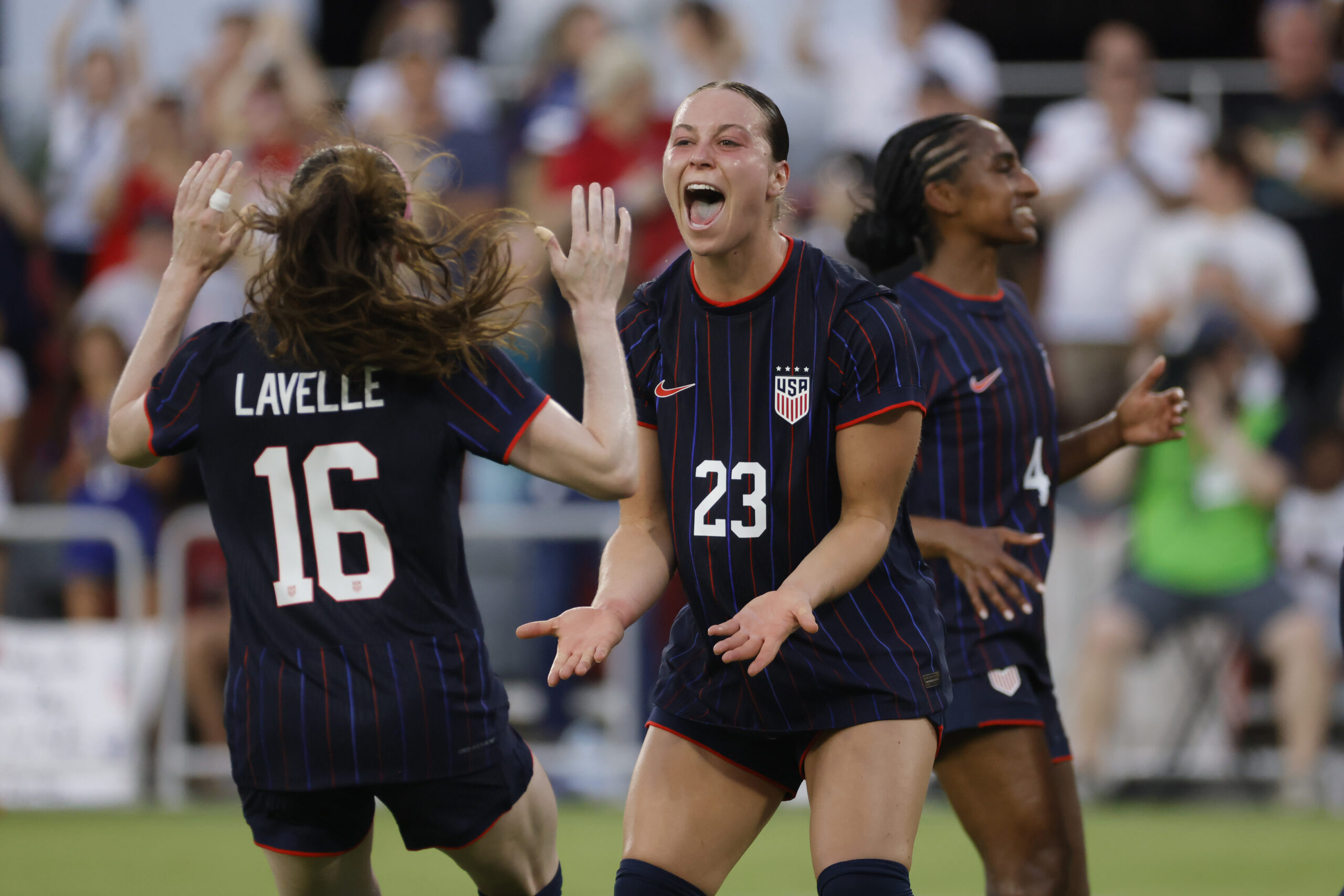 Two players celebrate on the field in blue jerseys after a goal is scored