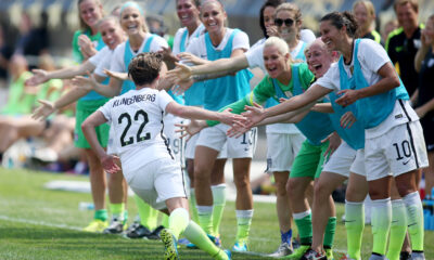 USWNT defender Meghan Klingenberg runs down the sideline, high-fiving teammates. She is facing away from the camera.